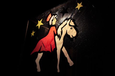 Ein farbenfrohes Bild einer Figur in einem roten Kleid, die ein Pferd reitet. Im Hintergrund sind Sterne zu sehen.