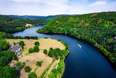 Een schilderachtig landschap met een rivier, omgeven door groene heuvels en bossen. Een klein bootje vaart rustig over het water.