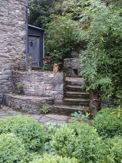 Ein schöner Garten mit steinernen Stufen und viel grünem Pflanzbewuchs. Im Hintergrund ist eine Gebäudefassade sichtbar.