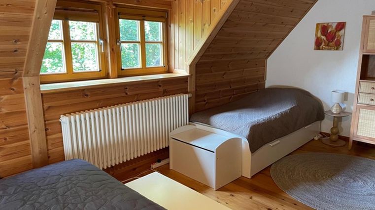 Een gezellige slaapkamer met houtbekleding en twee eenpersoonsbedden. Er zijn ramen met uitzicht op het groen en een ronde tapijt op de vloer.