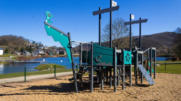 Ein ruhiger Park mit einem Teich und grünem Gras. Im Hintergrund sind Bäume und sanfte Hügel zu sehen.