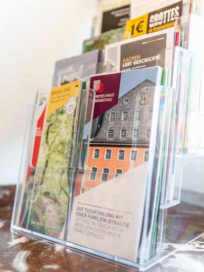 Ein Flyer-Ständer mit verschiedenen Broschüren über lokale Sehenswürdigkeiten und Geschichtsthemen. Die Broschüren sind farbenfroh und informativ gestaltet.