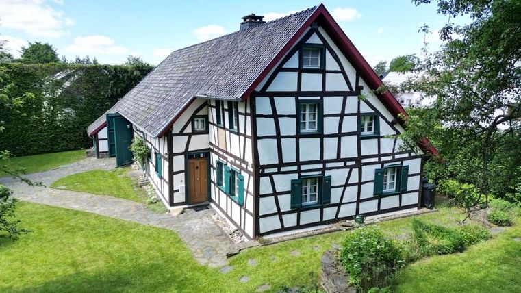 Ein hübsches Fachwerkhaus mit einem roten Dach und grünen Fenstern. Der Garten um das Haus herum ist gepflegt und grün.