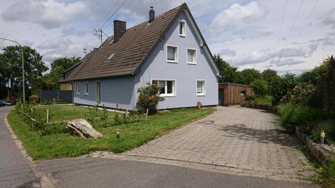 Ein modernes, französisches Haus mit blauer Fassade steht an einer ruhigen Straße. Der Garten ist grün und gepflegt, mit einem gepflasterten Weg zur Zufahrt.