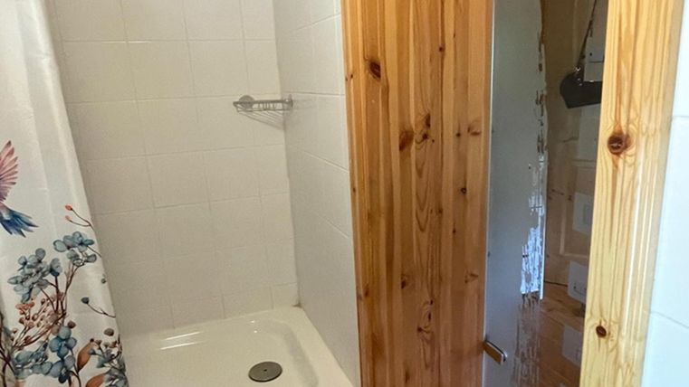 Een eenvoudige douche met witte tegels en een met hout beklede ingang. De douchegordijn toont een floraal ontwerp.
