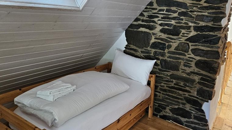 Ein gemütliches Schlafzimmer mit einem Holzbett und frischen Handtüchern. Die Wände sind teilweise mit Naturstein verkleidet, was einen rustikalen Charme verleiht.