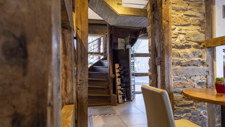 Ein gemütlicher Innenraum mit rustikalen Holzwänden und einem Treppenaufgang. Auf einem Tisch steht eine kleine Pflanze.