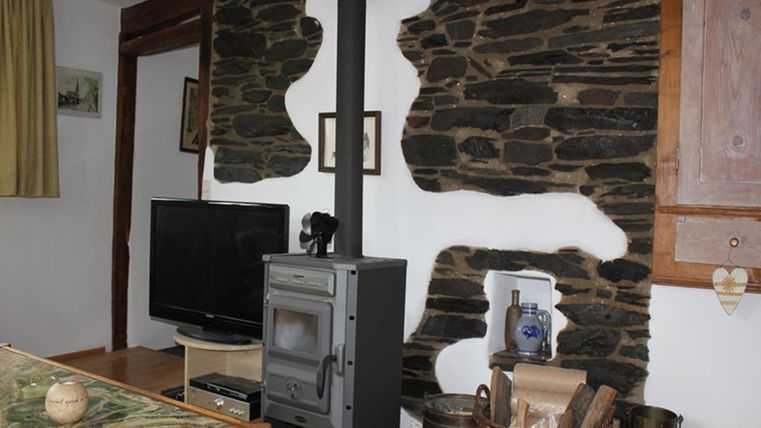 Ein gemütlicher Wohnraum mit einem modernen Ofen und einem Fernseher. Die Wände sind mit natürlichen Steinen dekoriert, was eine rustikale Atmosphäre schafft.