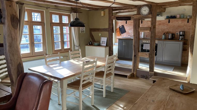 Eine gemütliche Küche mit einem großen Esstisch und Stühlen. Helle Fenster sorgen für viel natürliches Licht.