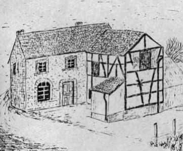 Ein historisches Haus mit Steinfassade und einem Fachwerkgebäude daneben. Die Umgebung wirkt ländlich und einfach.