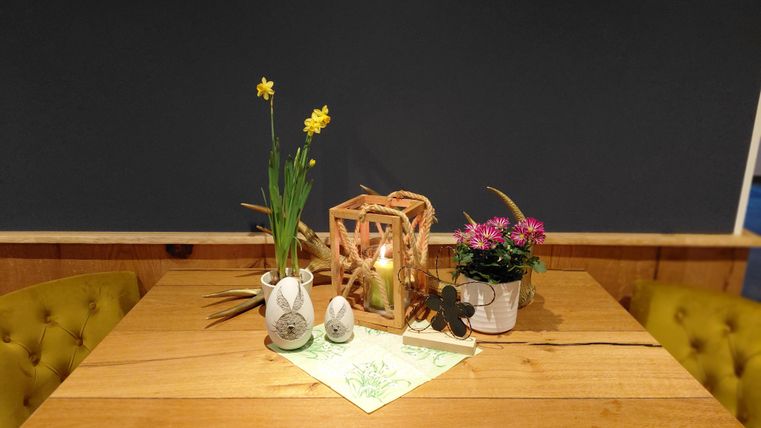 Ein schön dekorierter Tisch mit gelben Stühlen. Auf dem Tisch stehen Pflanzen, eine Laterne und dekorative Ostereier.