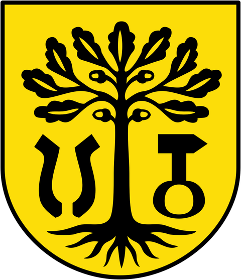 Ein Wappen mit einem schwarzen Baum auf gelbem Hintergrund. Neben dem Baum befinden sich symmetrische, stilisierte Symbole.