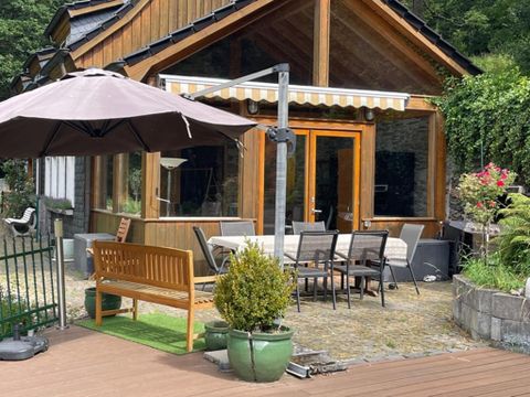 Een gezellig houten huis met een terras en een parasol. Er zijn stoelen en een tafel buiten om van de natuur te genieten.