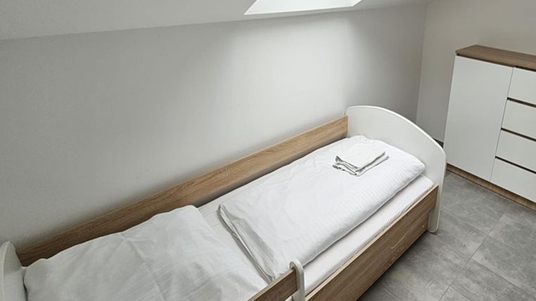 Ein schlichtes Zimmer mit einem Einzelbett und einem Schrank. Es hat einen hellen, modernen Look und einen Dachfenster.