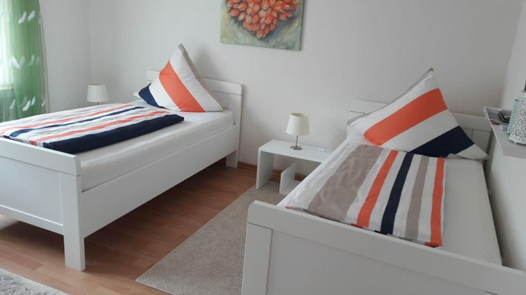 Ein gemütliches Schlafzimmer mit zwei Einzelbetten und bunten Kissen. An der Wand hängt ein Kunstwerk in Herzform.