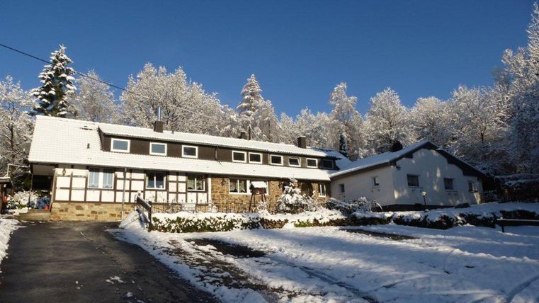 Ein schneebedecktes Gebäude in einer winterlichen Landschaft. Bäume sind mit Schnee bedeckt und der Himmel ist klar und blau.