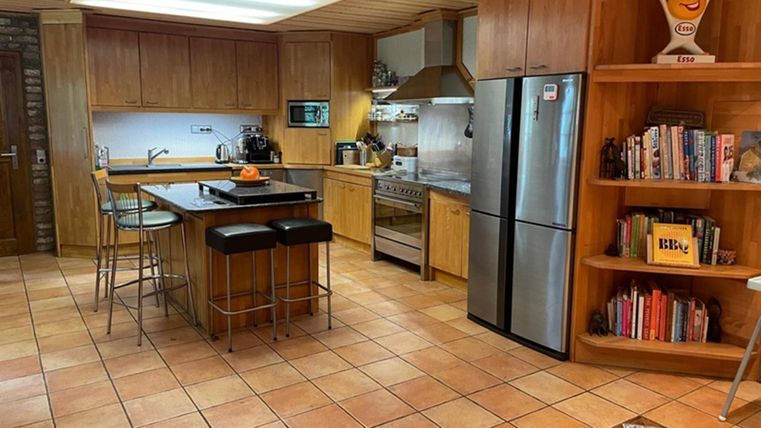 Een moderne keuken met houten meubels en een groot raam.
De ruimte is goed verlicht en heeft een eetgedeelte met hoge stoelen.