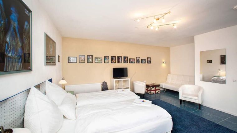 Ein modernes Hotelzimmer mit zwei Einzelbetten und eleganter Einrichtung. An den Wänden hängen verschiedene Bilder, und es gibt einen Fernseher sowie eine gemütliche Sitzecke.