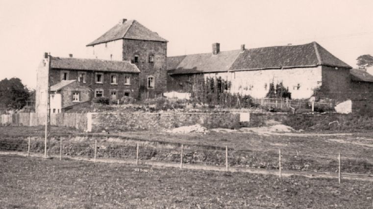Une ferme historique dotée d'un grand jardin aménagé. À l'arrière-plan, on aperçoit d'autres bâtiments, au cœur d'un cadre champêtre.