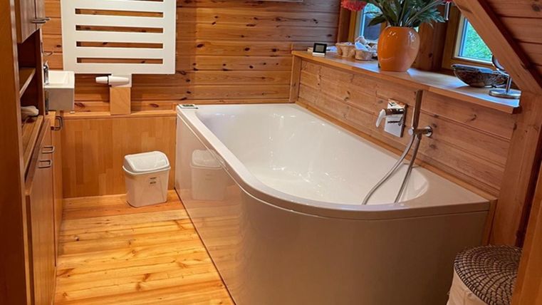 Een moderne badkamer met een vrijstaande badkuip en houten bekleding. De inrichting is helder en uitnodigend, met planten en natuurlijk licht.