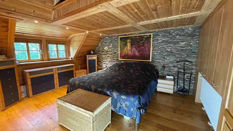 Een gezellig slaapkamer met houten panelen. Er is een groot bed, een rieten tafel en een kunstwerk aan de muur.