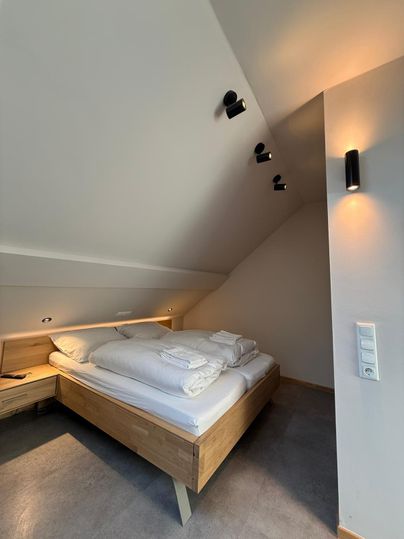 Une chambre moderne avec un lit en bois et du linge de lit frais. Les murs sont clairs, et l'éclairage est chaud et accueillant.