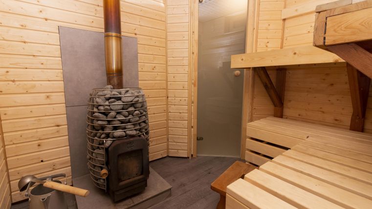 Eine gemütliche Sauna mit Holzverkleidung und einem steinernen Ofen. Die Bänke sind aus hellem Holz und der Raum strahlt Wärme aus.