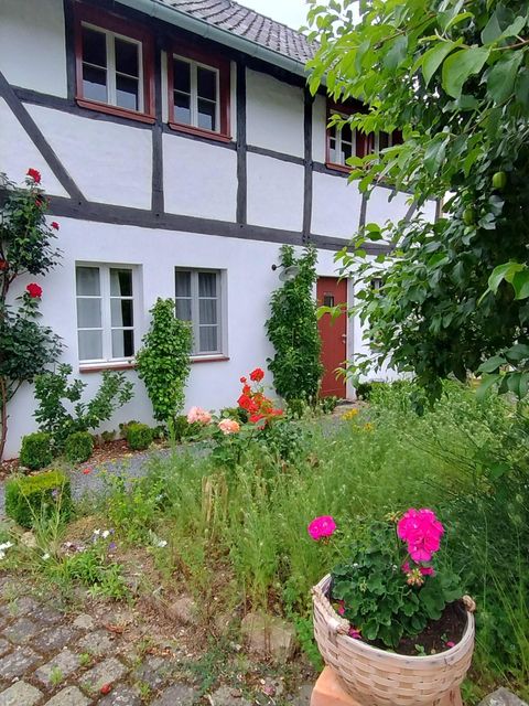Une maison à colombages traditionnelle avec un jardin bien entretenu. Des fleurs colorées et des plantes vertes décorent l'entrée.