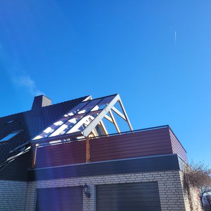 Ein modernes Haus mit einem sichtbaren Dachstuhl und einem blauen Himmel. Die Fassade ist in hellen Farbtönen gehalten.