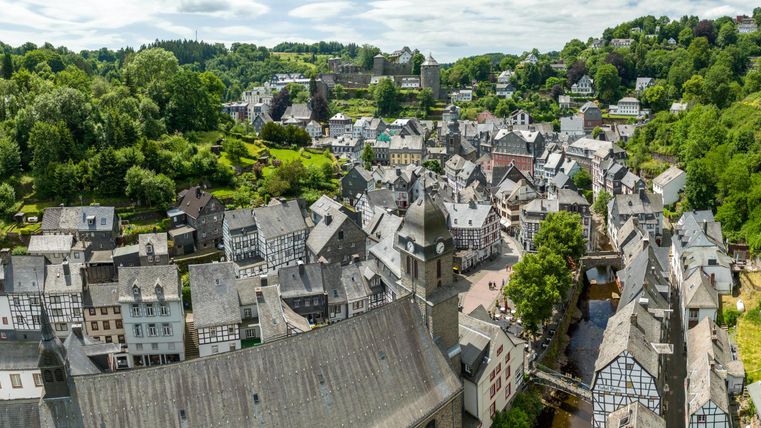 Eine malerische Stadt mit traditionellen Häusern und grünen Hügeln im Hintergrund. Der Himmel ist bewölkt und die Landschaft wirkt friedlich.