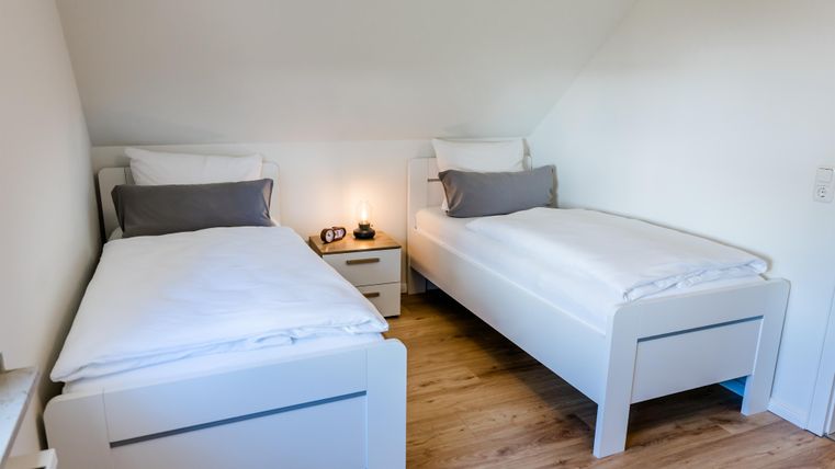 Ein modernes Schlafzimmer mit zwei Einzelbetten. Der Holzfußboden und die hellen Wände schaffen eine einladende Atmosphäre.