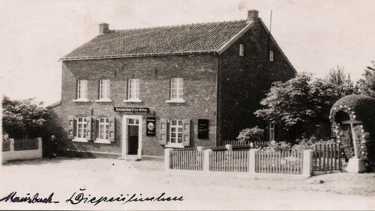 Een oud, gemetseld huis met witte ramen en een boerderijachtige charme. Voor het huis staan bomen en is een tuin met een hek te zien.