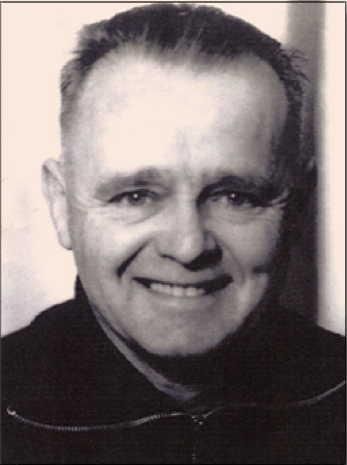 An older man with a friendly smile looks directly into the camera. He is wearing a dark sweater and looks well-groomed.