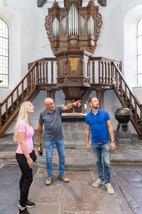 Ein Stadtführer erklärt zwei Personen Fakten in einer Kirche in Stolberg
