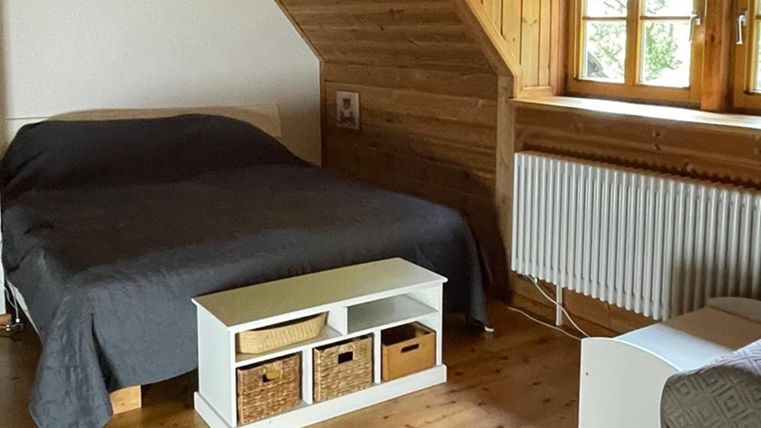 Een gezellige slaapkamer met een tweepersoonsbed en houten details. De ruimte heeft grote ramen en een moderne commode.