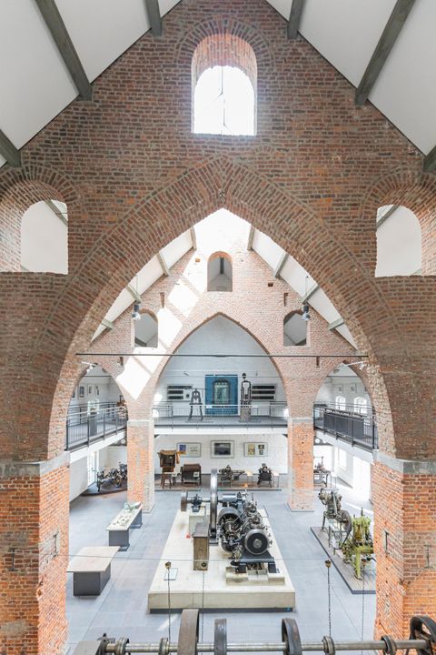 Ein historisches Industriedenkmal mit hohen, gewölbten Wänden aus Backstein. Im Inneren sind Maschinen und Ausstellungsobjekte in einer offenen Layout angeordnet.
