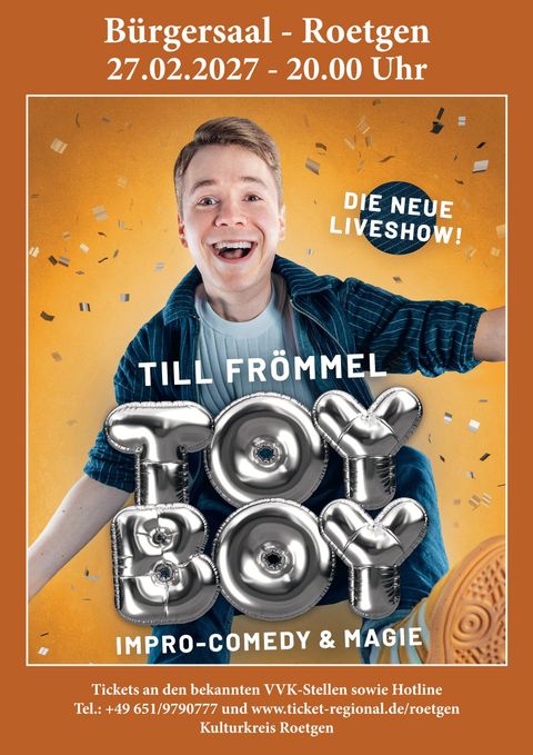 A cheerful man with a broad smile is promoting his new live show "Toy Boy". The event takes place on the 27th of February 2027 in the Bürgersaal Roetgen.