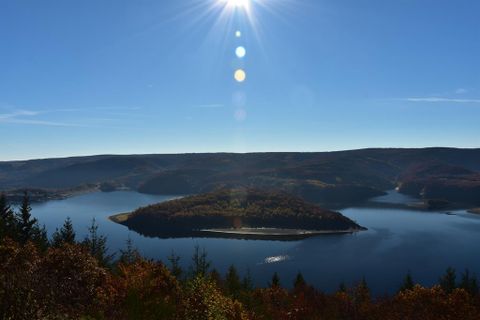 Eine malerische Landschaft mit einem klaren See und einer kleinen Insel. Die Sonnenstrahlen reflektieren sich auf dem Wasser und umgeben von buntem Herbstlaub.