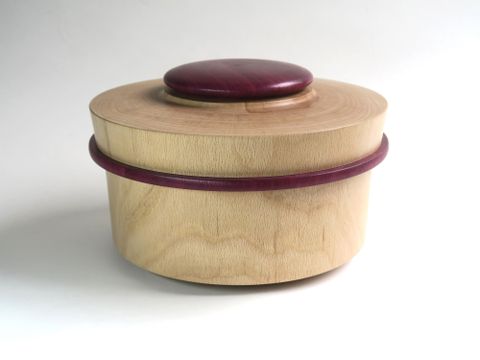 Eine wunderschöne Holzkiste mit einem runden Deckel. Die Kiste hat eine helle Farbe und einen lila Akzent.