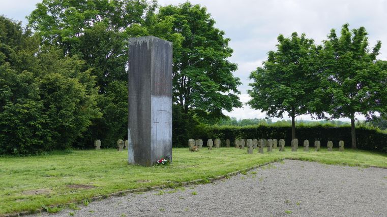 Un monument en pierre se dresse dans un pré verdoyant, entouré d'arbres. De petites pierres sont disposées tout autour du monument.