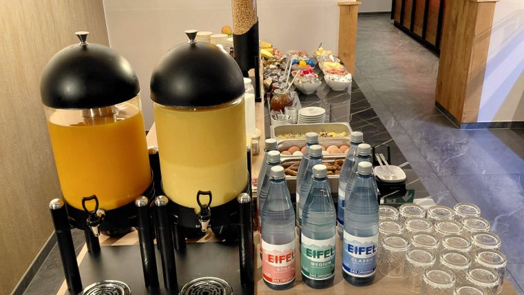 Een selectie van drankjes, waaronder sap en mineraalwater, staat op een tafel. Op de achtergrond zijn verschillende snacks en glazen te zien.