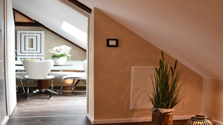 Une charmante pièce sous les toits avec des murs en pente. À l'arrière-plan, on peut voir un coin repas avec une table et des chaises.