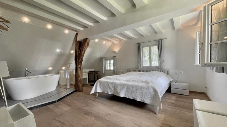 Ein modernes Schlafzimmer mit einem großen Bett und einer freistehenden Badewanne. Helle Wände und holzige Akzente schaffen eine einladende Atmosphäre.