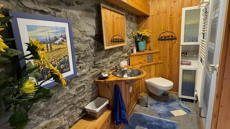 Een gezellig badkamer met houten meubels en stenen wanden. Er is een wastafel met spiegel en decoraties van bloemen.
