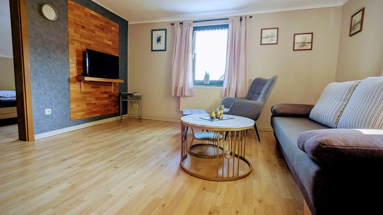 Ein gemütliches Wohnzimmer mit Holzfußboden und modernen Möbeln. Es gibt ein Sofa, einen Tisch und einen Fernseher an der Wand.