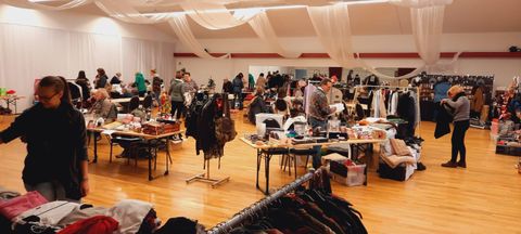 Ein belebter Flohmarkt mit Tischen voll Kleidung und verschiedenen Gegenständen. Viele Menschen stöbern und kaufen in einer gemütlichen Atmosphäre.