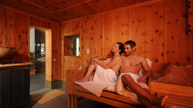 Ein Paar entspannt in einem Holzsauna-Raum. Die Atmosphäre ist gemütlich und einladend.
