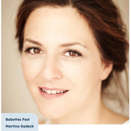 Ein Portrait einer lächelnden Frau mit strahlenden Augen. Der Hintergrund ist neutral, was den Fokus auf ihr Gesicht legt.