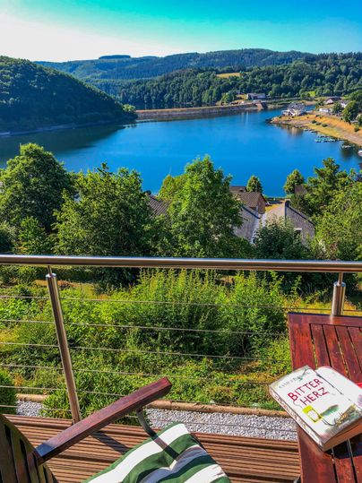 Eine schöne Aussicht auf einen klaren See umgeben von Bäumen. Auf einem Tisch liegt ein Buch, das zur Entspannung einlädt.