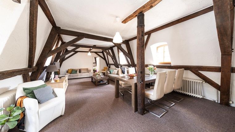 Ein geräumiges Wohnzimmer mit Holzrahmen und einem einladenden Esstisch. Die Einrichtung ist modern und hell, mit einem gemütlichen Sofa.